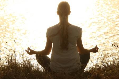 woman meditating next to a lake